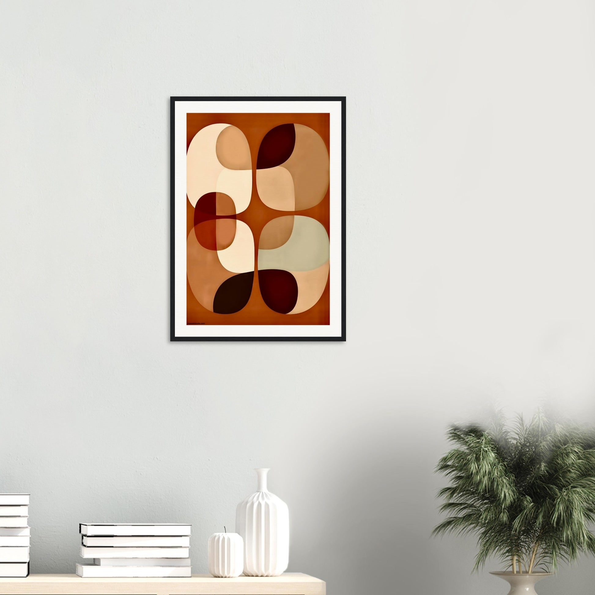 Framed abstract art print with soft earth tones on a wall with decorative items below.