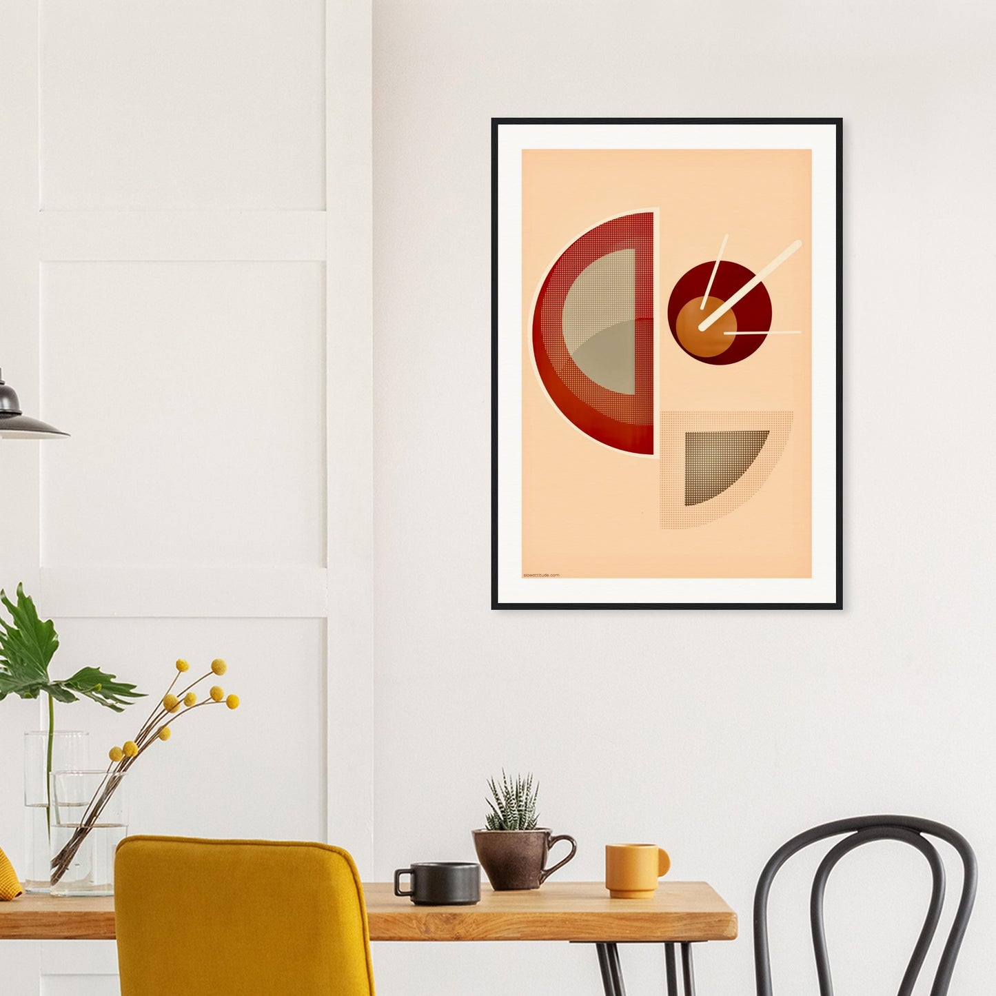 Framed abstract geometric art print on a wall above a table with chairs.