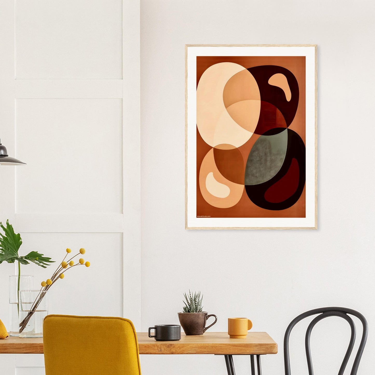 Abstract art print with natural wooden frame on a wall above a dining table with chairs.